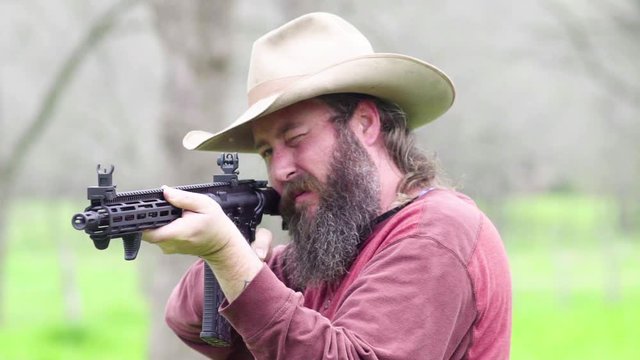Front angle of a cowboy shooting a high powered rifle on his property, slow motion 23.98 fps.