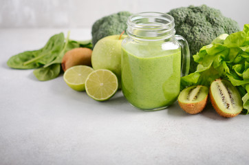 Fresh green smoothie in a jar with ingredients on a gray concrete background