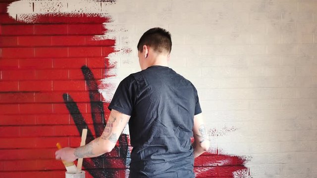 Person whitewashing a red painted brick wall