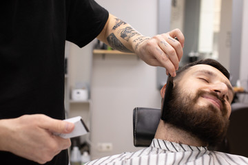 Naklejka na ściany i meble Client during beard shaving in barber shop 