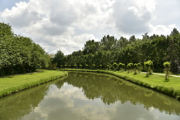 Fototapeta na wymiar Le chenal principal et sa rangée d'arbres minuscules le long d'un bois au domaine provincial de Vrijbroekpark à Malines