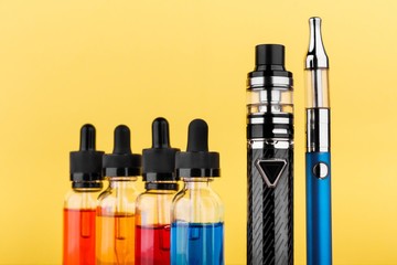 vaping devices and bottles with vape liquid on yellow background