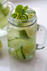a glass with water, mint, lime and cucumber on a white background.