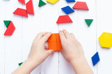 A child plays with colored blocks constructs a model on a light wooden background