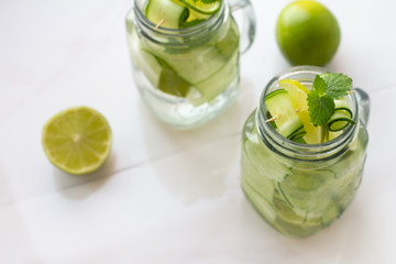 glasses with water, ice, mint, lime and cucumber and place for text on a white background.