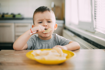 Hungry child eats Ukrainian dumplings in the kitchen, sitting on a chair in a gray t-shirt