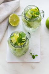glasses of water, mint, lime and cucumber on a white board and napkin.