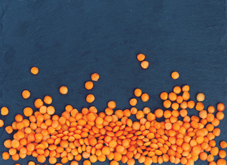 Orange lentil lies on a black stone background.
