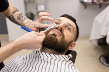 Obraz na płótnie Canvas Shaving process of beards in Barbershop. Master makes a haircut beard client with vintage straight razor. 