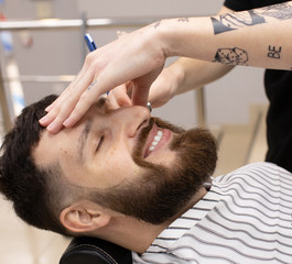 Obraz na płótnie Canvas Shaving process of beards in Barbershop. Master makes a haircut beard client with vintage straight razor. 