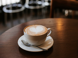 One cup of cappuccino with latte art on wooden table, white ceramic cup, place for text. Cafe culture.