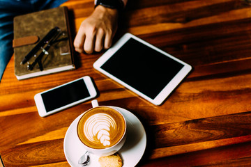 The hand of a man sitting at a table with a cup of aromatic coffee, a telephone and a notebook. Business lunch