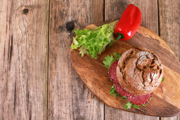 whole-grain bun topped with salad and salami sausage - freshly baked whole grain bun breakfast on rustic wooden table 