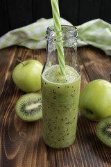 Smoothies with kiwi and green apples in the glass bottle on the brown  wooden background