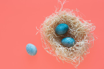 Blue Easter eggs lie in a nest on a coral background. Top view