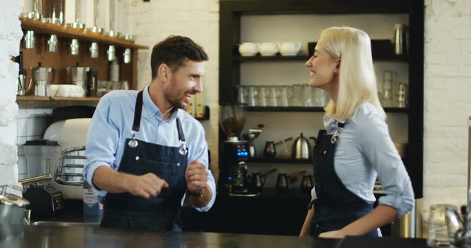 Young caucasian attractive man and woman working at the cafe as waiter and waitress, having fun and dancing while bar being empty.