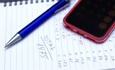 Phone calculator, notebook with calculations written by hand.