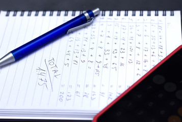 Phone calculator, notebook with calculations written by hand.