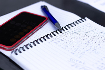 Phone calculator, notebook with calculations written by hand.