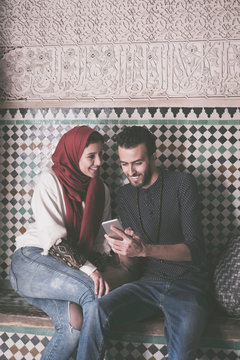 Young Muslim Couple Smiling And Looking At Mobile Phone