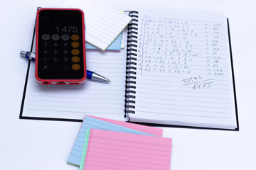 Phone calculator, notebook with calculations written by hand.