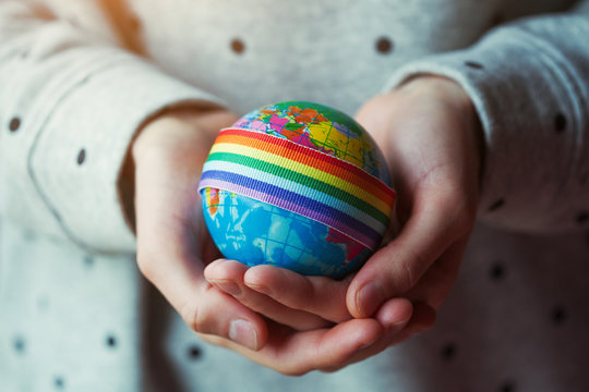woman's hands holding globe with LGBT rainbow ribbon, gay pride, gender equality problems, bisexual, homosexual people concept
