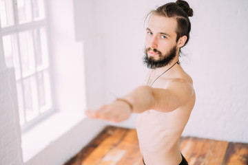 Young sporty man doing yoga in studio, with wooden floor and big windows. Freedom, health and yoga...