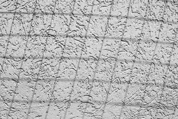 A black and white photograph of the exterior concrete wall of the house with a rubbing and shadow from the grid