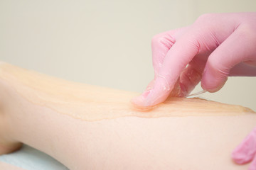 procedure of hair removing on leg beautiful woman with sugar paste or wax honey and pink gloves hand - depilation and beauty concept