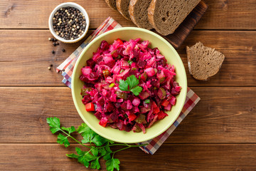 Traditional russian salad vinaigrette with boiled vegetables, pickled cucumbers and sauerkraut in bowl on wooden table. Top view. Copy space.