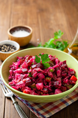 Traditional russian salad vinaigrette with boiled vegetables, pickled cucumbers and sauerkraut in bowl on wooden table. Selective focus.