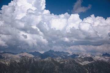 Fototapeta premium The peaks of the Caucasus Mountains in cloudy clouds and the rays of the sun through them in the outskirts of Dombai. And on the tops of snow lies.