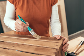 Female carpenter varnishing wooden crate with brush