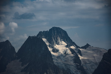 The peaks of the Caucasus Mountains in cloudy clouds and the rays of the sun through them in the outskirts of Dombai. And on the tops of snow lies.