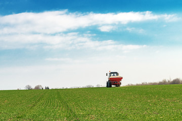 Agricultural tractor fertilizing wheat crop field with NPK