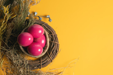 Fototapeta na wymiar easter eggs pink on yellow background with spoon and fork and dried grass with wood vine and flower