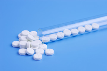 Medicine white pills in the test tube on blue background. Copy space for text