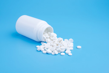 Medicine white pills or tablets drop out of the white bottle on blue background