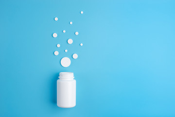 Medicine white pills or tablets drop out of the white bottle on blue background