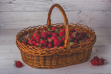 Wicker basket filled with ripe strawberries. On a white wooden background.