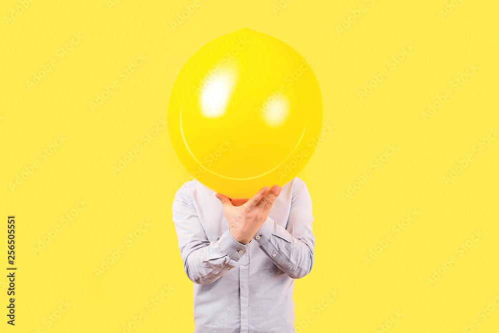 Wall mural man holding yellow balloon with smile face emotion instead of head. positive thinking concepts, imag