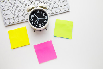 Office desk table with keyboard and alarm clock on white background, stickers yellow, purple and green color. Top view and copy space, flat lay