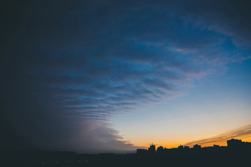 Cityscape with wonderful varicolored vivid dawn. Amazing dramatic blue cloud sky above dark...