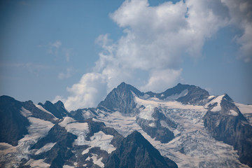 The peaks of the Caucasus Mountains in cloudy clouds and the rays of the sun through them in the outskirts of Dombai. And on the tops of snow lies.