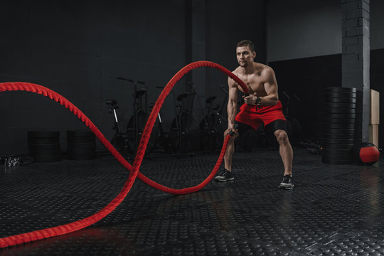 Young athlete doing battle ropes exercise at the crossfit gym