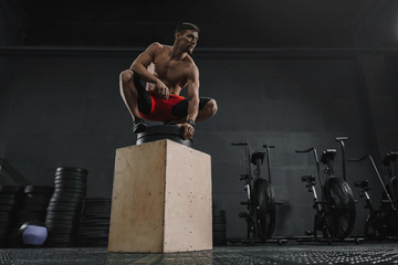 Young sportive man resting after box jump exercise at the gym