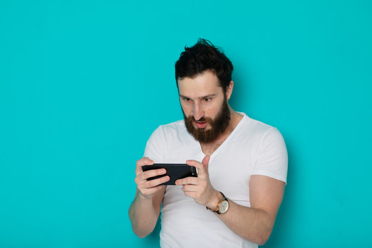 Portrait Of A Surprised Casual Man Looking At Mobile Phone Isolated Over Blue Background 