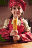 Adorable attractive beautiful caucasian child girl chef having fun and praparing vermicelli. Cooking process and food concept.