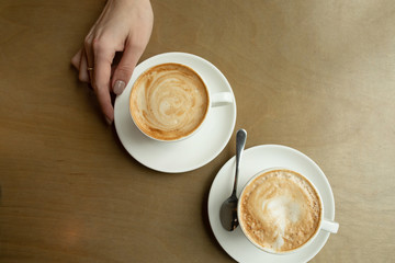 Two cups of cappuccino with latte art in white cups on wooden table. Morning coffee for couple in love. Top view. 