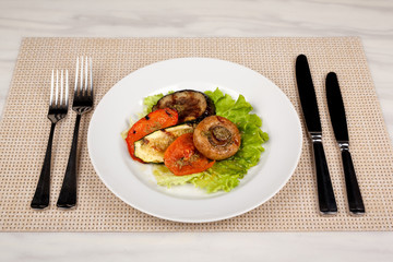 Fried mushroom champignon, eggplant, tomato and green leaf lettuce on a white round plate.